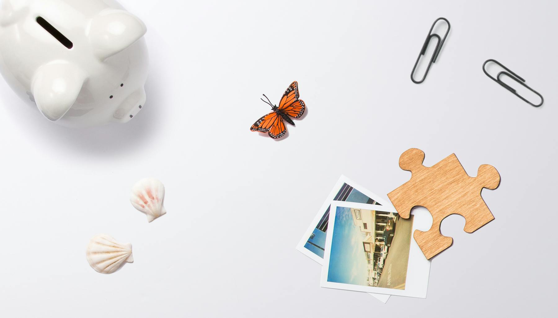 Flat lay of everyday objects representing personal finance and life decisions, including a piggy bank, seashells, a butterfly and photographs
